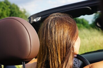 Closeup shot of a female with light brown hair driving in a convertible car under the sun