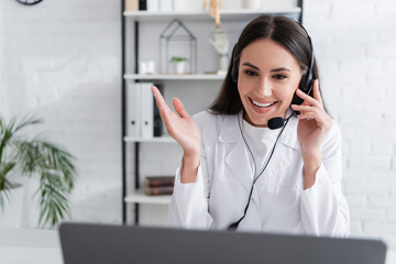 Smiling doctor in headset having video consultation on laptop in clinic