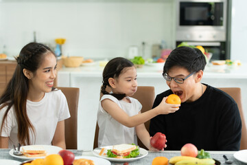 Asian father and mother Show your love to little daughter and having breakfast together happily in the dining room of the house.