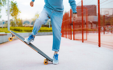 Young millennial man riding skateboard in city park at sunset. Outdoor activity and skateboarding