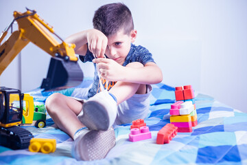 child tying shoes with hands on bed in his room among the toys