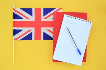 Flag of Great Britain, notebook and textbook on yellow background. Travel and learning foreign...