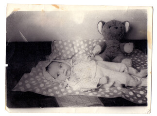 Vintage photo of little baby girl with teddy bear toy lying down
