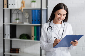 Cheerful doctor writing on clipboard in hospital