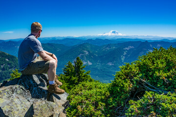 An athletic adventurous male hiker sitting on top of a mountain looking out at a mountain range on...