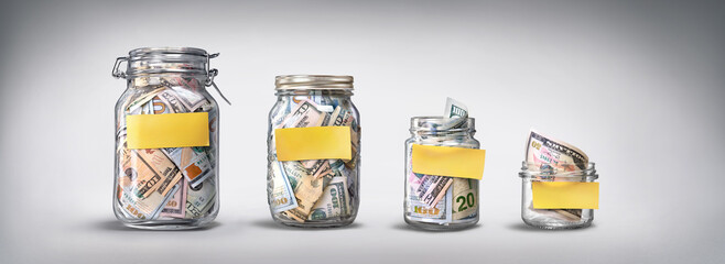 Four glass jars with yellow blank stickers, savings, cash money (dollar banknotes) on grey background