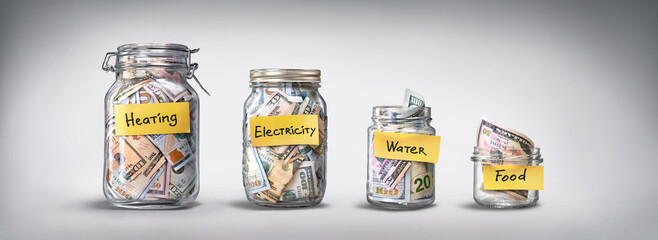 Four glass jars for savings, cash money (dollar banknotes) on grey background. For utility bills: heating, electricity, water. Savings for life and food