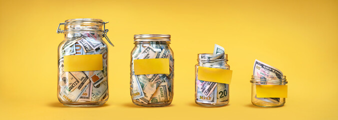 Four glass jars with yellow blank stickers, savings, cash money (dollar banknotes) on yellow...