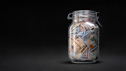 Glass jar with savings (dollar banknotes) on black background