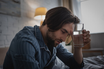 Tired man in pajama holding glass of water in bed in morning