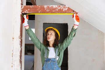 Live portrait of young woman, builder wearing helmet using different work tools at a construction...