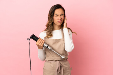 Young woman using hand blender over isolated pink background frustrated and covering ears