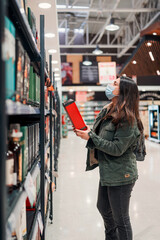 mature latin woman with mask choosing or buying drink in a supermarket