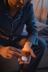 Cropped view of man with sleep disorder holding pills on bed at night