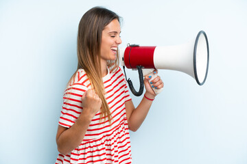 Young caucasian woman isolated on blue background shouting through a megaphone to announce something in lateral position