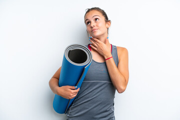 Young sport woman going to yoga classes while holding a mat isolated on white background looking up while smiling
