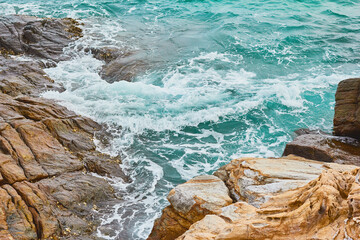 Turquoise rolling wave slamming on the rocks of the coastline.