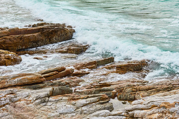 Turquoise rolling wave slamming on the rocks of the coastline.