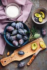 Fresh blue plums in a bowl and chopped plums on chopping board.