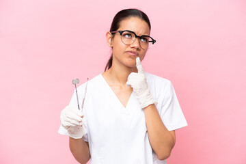 Dentist Colombian woman isolated on pink background having doubts while looking up