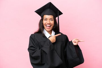 Young university Colombian woman graduate isolated on pink background surprised and pointing side