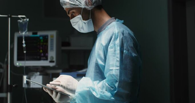 A male doctor in sterile clothing uses a digital tablet in intensive careo