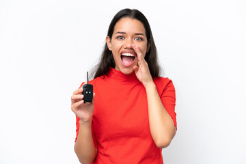 Young Colombian woman holding car keys isolated on white background shouting with mouth wide open