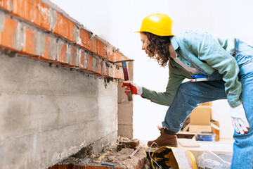 Live portrait of young woman, builder wearing helmet using different work tools at a construction...