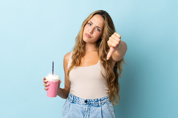 Young woman with strawberry milkshake isolated on blue background showing thumb down with negative expression