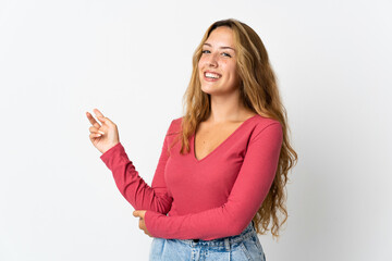 Young blonde woman isolated on blue background happy and pointing up