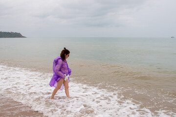 Fototapeta na wymiar A girl in a raincoat enters the sea