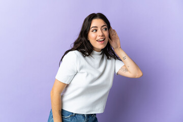 Young caucasian woman isolated on purple background listening to something by putting hand on the ear