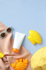 Flat lay baby sunscreen lotion tube, sunglasses, towel, panama hat, sand molds on blue table.