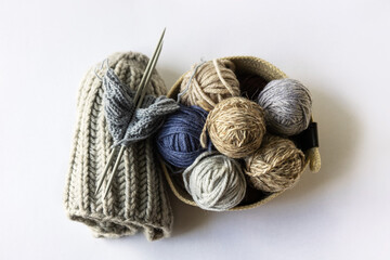 Fototapeta na wymiar Gray, brown and blue balls of knitting threads in a beige basket with knitting needles and knitted hats for winter and autumn, knitting hobby