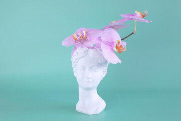 Creative concept colorful head of an ancient statue, hair made of fresh flowers. Plaster sculpture of woman's face on background of an orchid. Romantic surreal concept of spring-summer fashion vision
