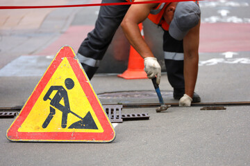 Road works sign, worker of municipal services repairs drainage system. Wastewater treatment, orange...