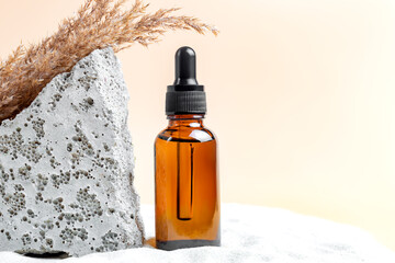 cosmetic bottle with serum or essential oil on sand background. Natural cosmetics, summer vacation concept. Stone and dry reeds decoration. Mock up.