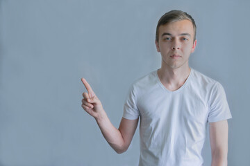 Young handsome man wearing casual white shirt pointing something on his side with his hand over gray background