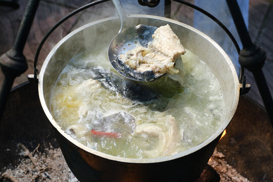 Cooking delicious fish soup or uha on a fire. Cast iron cauldron with boiling fish broth and sturgeon. Shallow depth of field.