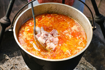 Cast iron cauldron with boiling fish soup. Cooking delicious fish broth with sturgeon, and vegetables. Shallow depth of field.