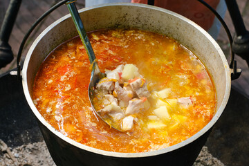 Cooking fresh-soup fish soup or uha on a fire. Cast iron cauldron with boiling fish broth. Delicious fish broth with sturgeon, and vegetables. Shallow depth of field.