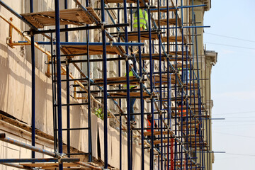 Scaffolding on the old building facade. Workers repair house wall, applying cladding and plastering