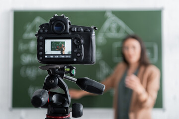 Blurred teacher standing near chalkboard and digital camera