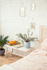 Bright bedroom with a wooden bedside table, a book and plants on it