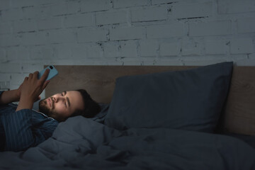 Young man using smartphone on bed at night