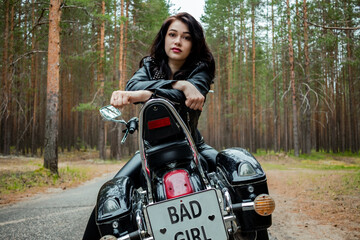 Fototapeta na wymiar A girl in tight black leather sits on a motorcycle.