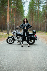 Fototapeta na wymiar A girl in tight black leather stands next to a motorcycle.