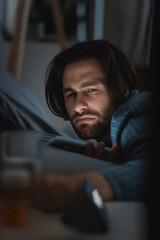 Obraz premium Dissatisfied man with insomnia holding smartphone on bed at home
