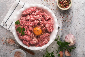 Raw minced meat. Ground meat beef, pork or lamb spices, herbs and eggs on white plate on light grey concrete background. Fresh minced meat ready for cooking. Food cooking background. Top view.