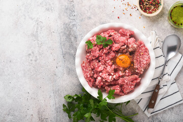 Raw minced meat. Ground meat beef, pork or lamb spices, herbs and eggs on white plate on light grey concrete background. Fresh minced meat ready for cooking. Food cooking background. Top view.